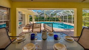 Comedor con mesa dispuesta para cuatro, con vista a una piscina y abundante follaje.