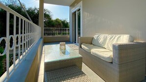 A balcony with a wicker sofa and a glass table, a white railing, and a view of greenery. - Elysian Luxury Studio 4 (Roda, Corfu)