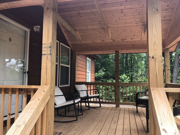 A wooden deck with two chairs and a table, overlooking a forested area.