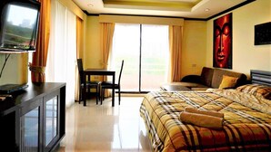 A hotel room with a bed, a television, a dining table with chairs, and a large window. - Angket Condominium Corner Apartment With Large Balcony (Pattaya)