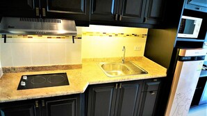 A kitchen with black cabinets, a stainless steel sink, a built-in microwave, and a range hood. - Angket Condominium Corner Apartment With Large Balcony (Pattaya)