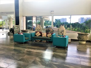 Een hal met smaragdgroene stoelen, grote vazen en een geruit sofa.