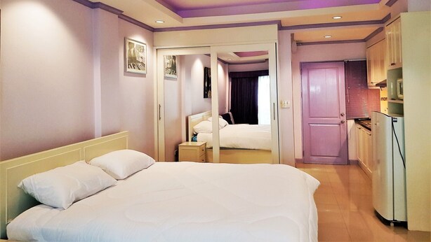 Habitación de hotel con una cama grande, ventilador de techo, kitchenette y un baño visible a través de una puerta abierta.