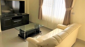 Un soggiorno con un mobile TV nero, un tavolino da caffè in vetro, un divano in pelle bianca e una grande TV a schermo piatto.