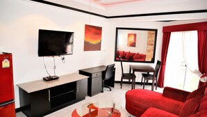A modern living room with a flat-screen TV, a red sofa, a glass coffee table, and a dining area with a red table and chairs.