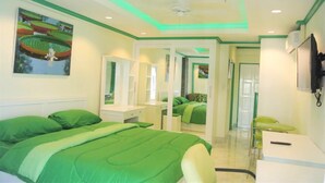 Une chambre avec un lit aux motifs verts, un ventilateur de plafond, un tableau et un miroir.