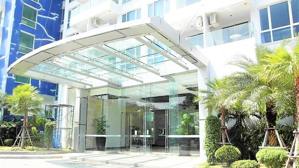 A modern hotel entrance with a glass facade, a covered entrance area, and surrounding greenery. - The Cliff sea & Pool Views Studio Apartment Pratumnak Pattaya (Pattaya)
