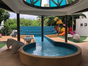 A pool area with a circular hot tub, seating, and a children's play area with slides.