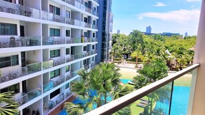 A high-rise hotel with multiple balconies, a pool area with palm trees, and a view of a cityscape in the background. - Laguna Beach 1A With Swimming Pool Views Pattaya (Pattaya)