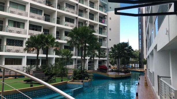 A modern hotel interior with a swimming pool, multiple balconies, and indoor plants. - Laguna Beach 1A With Swimming Pool Views Pattaya (Pattaya)
