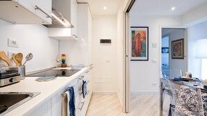 Une cuisine moderne avec des meubles blancs, des appareils en acier inoxydable et un coin repas délimité par une paroi en verre transparent.