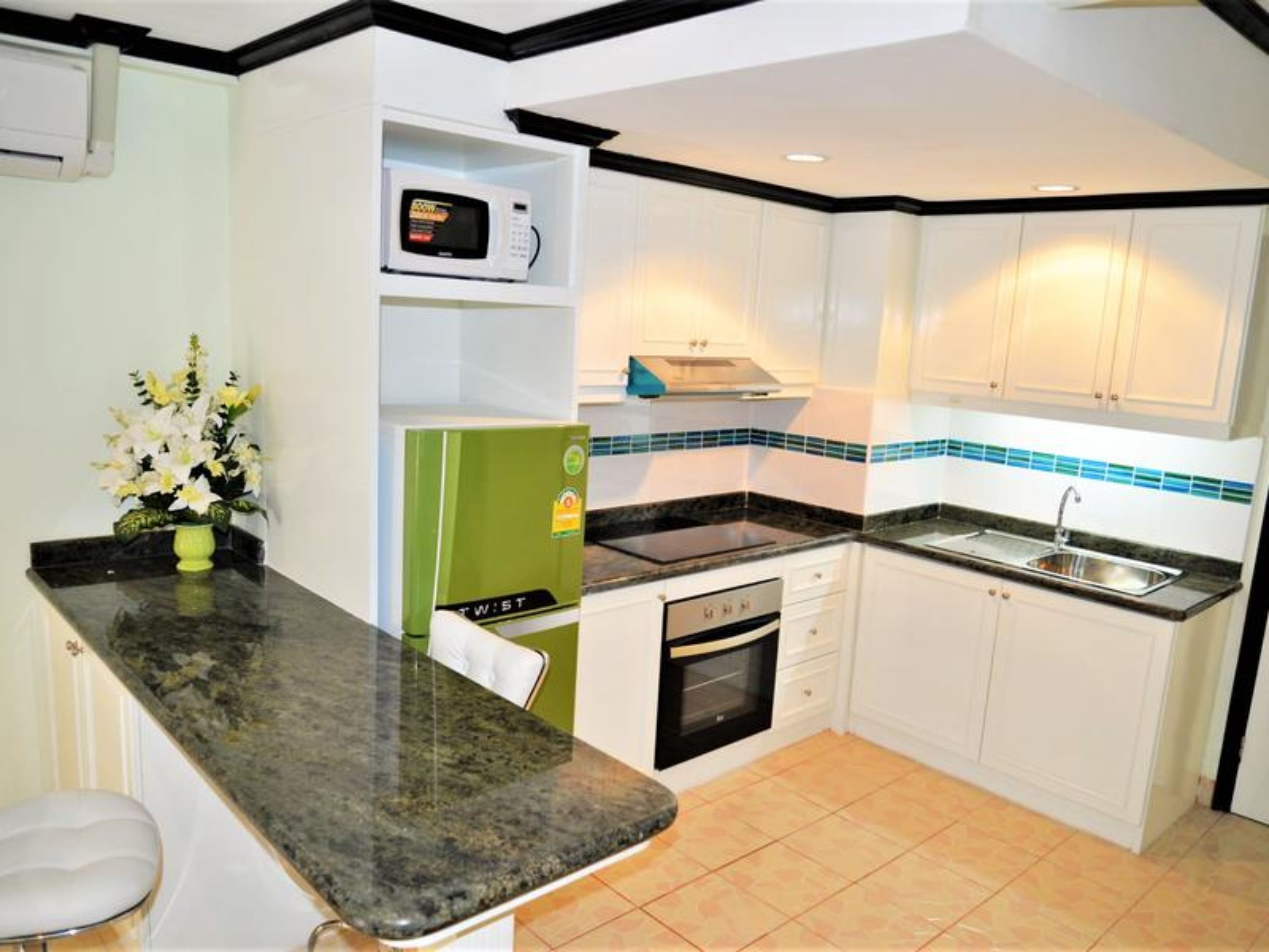 A compact kitchen with white cabinets, a black countertop, a microwave, a stove, and a sink.