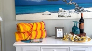 A white dresser with a painting of a beach scene above it, a bottle of wine, and a framed certificate on the dresser.