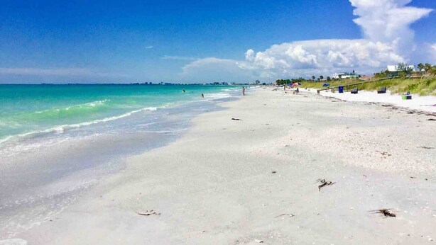 A beach with clear turquoise waters, a sandy shore, and a few people in the distance.