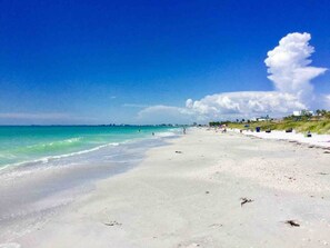 A beach with clear turquoise waters, a sandy shore, and a few people in the distance.