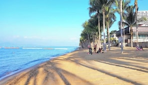 Una playa con palmeras, cielo despejado y un edificio con un letrero.