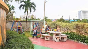 Un'area giochi con scivoli e altalene, un tavolo da picnic e un siepe.