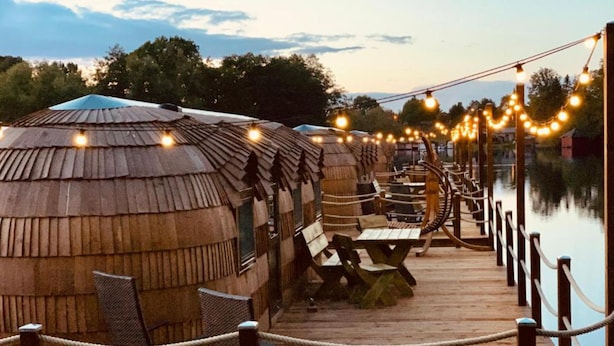 A wooden deck leading to thatched-roof huts with picnic tables and string lights. - Iglu Camp Templin (Templin)