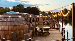 A wooden deck leading to thatched-roof huts with picnic tables and string lights. - Iglu Camp Templin (Templin)
