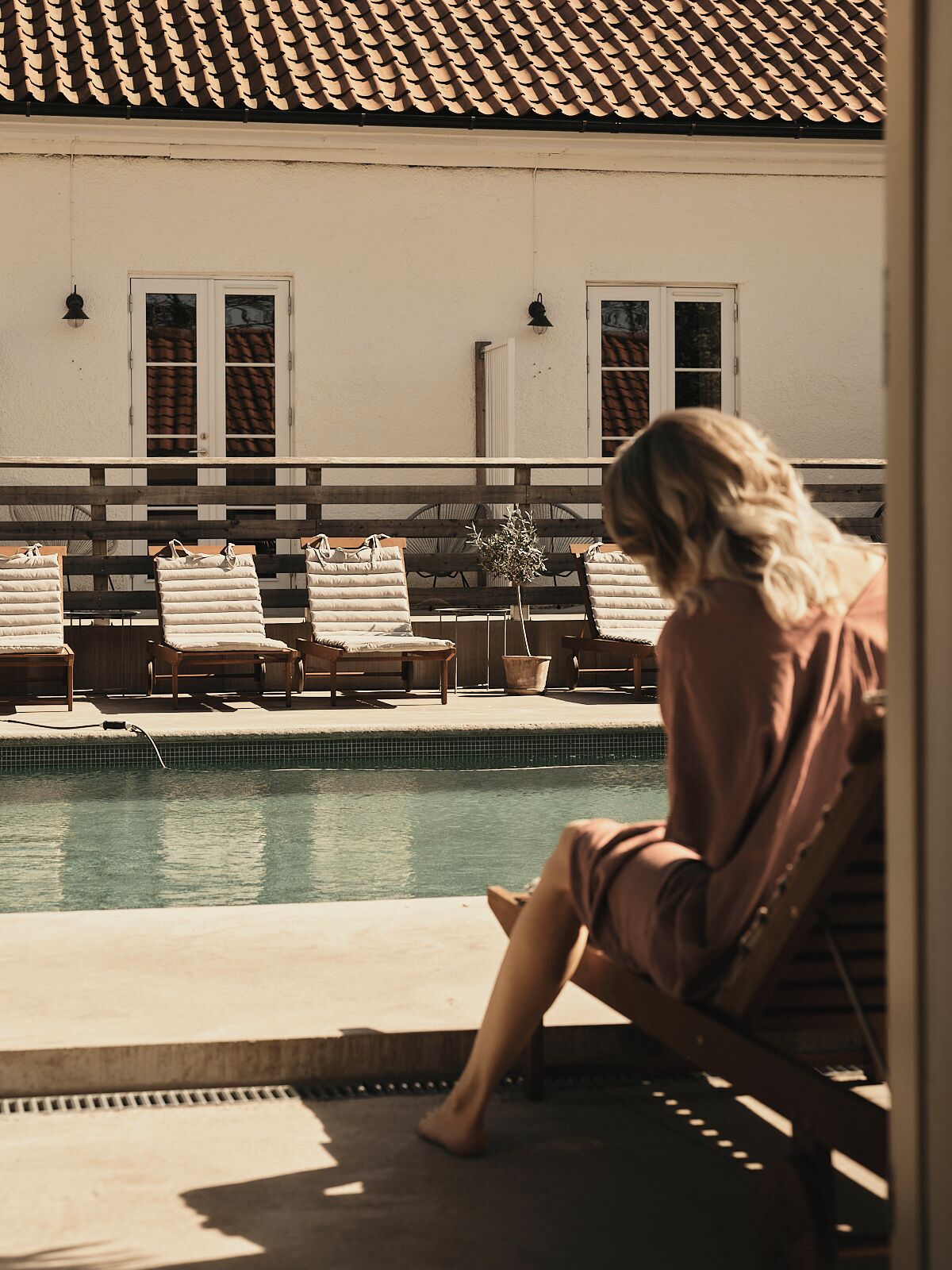 A poolside area with lounge chairs and a person sitting by the pool.