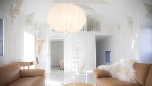 Une pièce spacieuse avec un plafond haut, un escalier en bois et un grand luminaire suspendu.