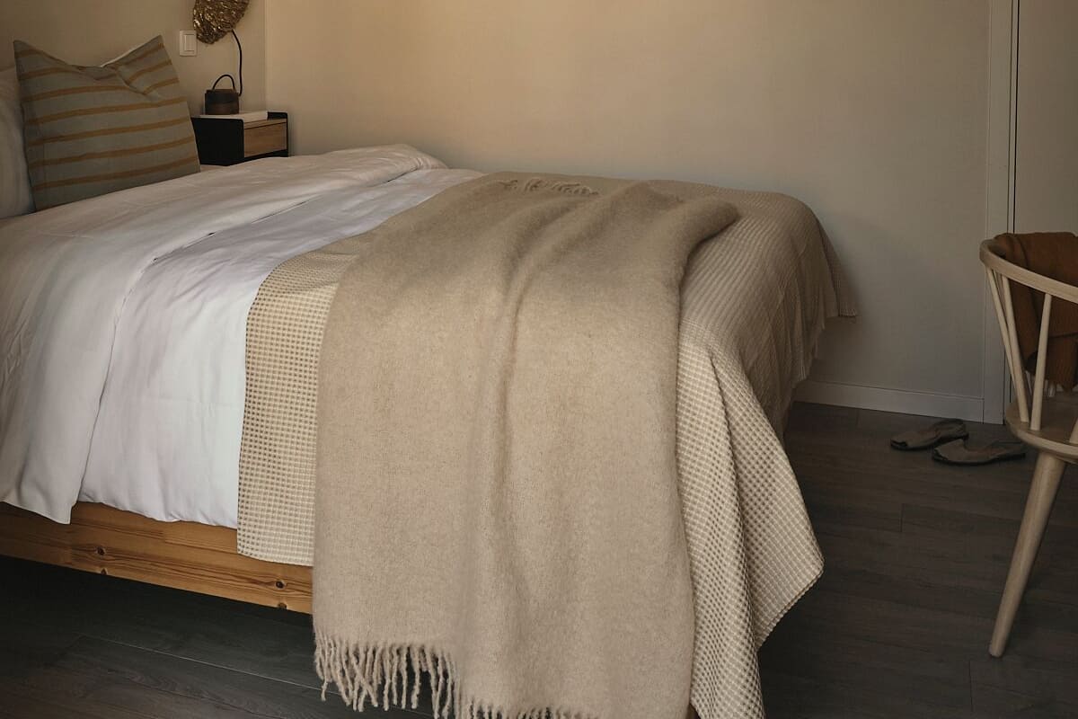 A bedroom with a wooden bed, a hanging light fixture, a small bedside table, and a chair.