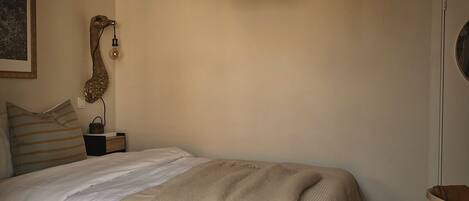 Una camera da letto con un letto in legno, una lampada a sospensione, un comodino e una sedia.
