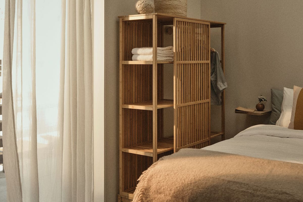 A bedroom with a bed, a wooden wardrobe, a bedside table, and a hanging light fixture.