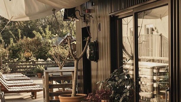 Un espace extérieur aménagé avec un banc et des plantes en pot, une table en bois et un grand parasol pour créer de l’ombre.