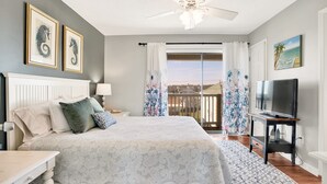 A bedroom with a bed, a TV, a ceiling fan, and a balcony with curtains.