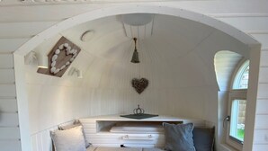 Un rincón acogedor para leer con techo abovedado blanco, un estante de madera con piedras decorativas, una lámpara colgante y un adorno de pared con forma de corazón.