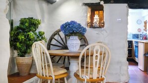 Zona pranzo rustica con tavolo in legno, due sedie di legno, un’ampia pianta in vaso e un vaso con fiori blu.
