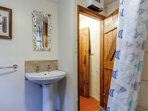 A bathroom with a pedestal sink, a mirror with a decorative frame, and a wooden door leading to another room.