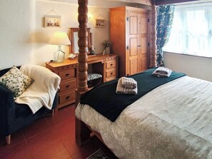 A bedroom with a four-poster bed, a desk with a lamp, a wardrobe, and a chair.