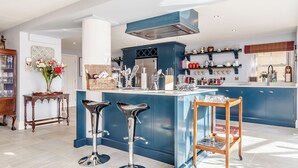 Een moderne keuken met blauwe kastjes, een centraal eiland met krukken, en diverse keukenapparaten en keukengerei.