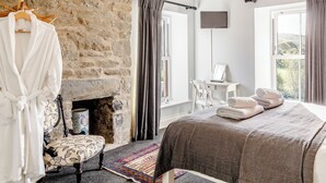 Een slaapkamer met een stenen muur, een open haard, een bed met handdoeken, een stoel, een bureau en een televisie.