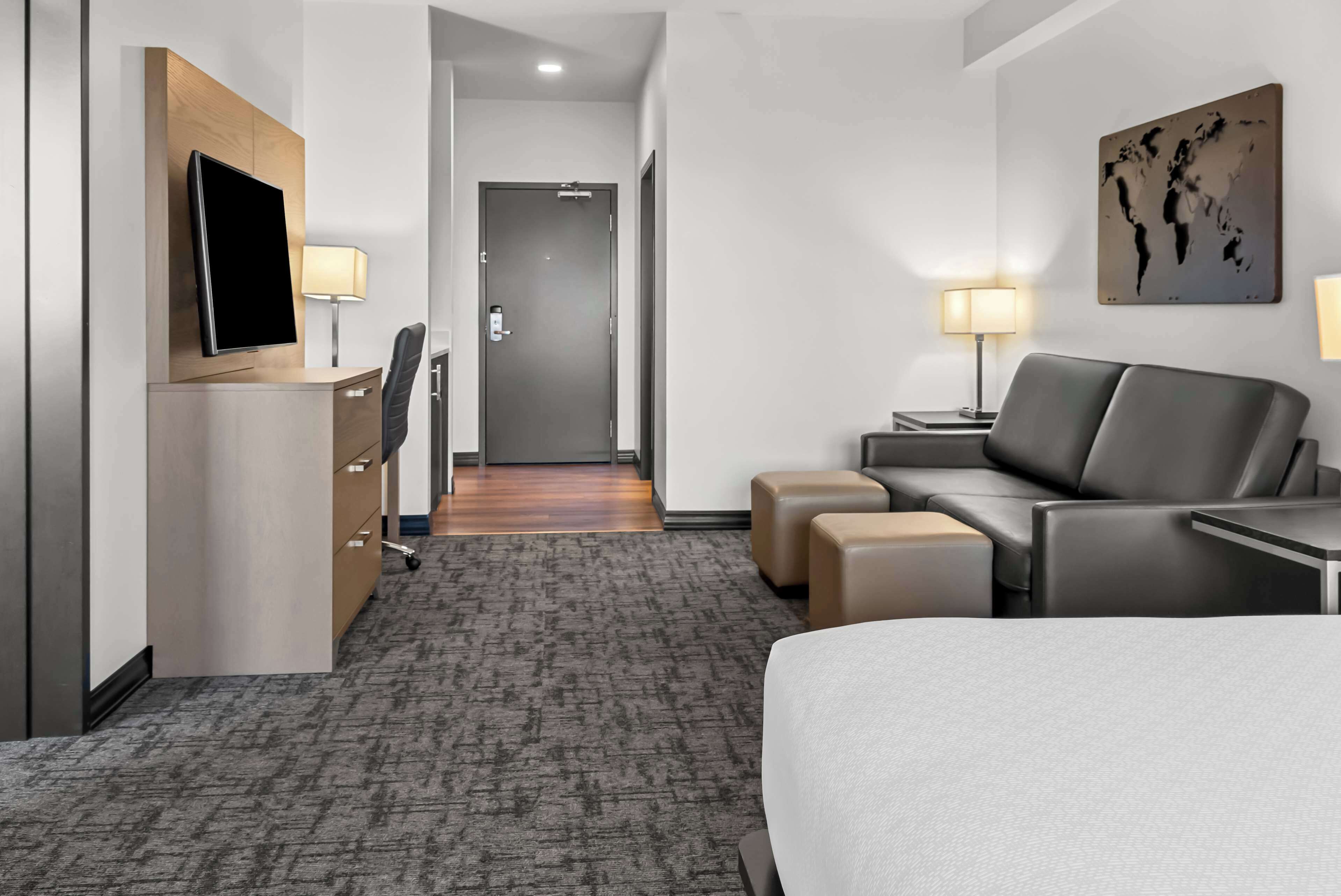A hotel room with a bed, a desk, a chair, a TV, and a lamp.
