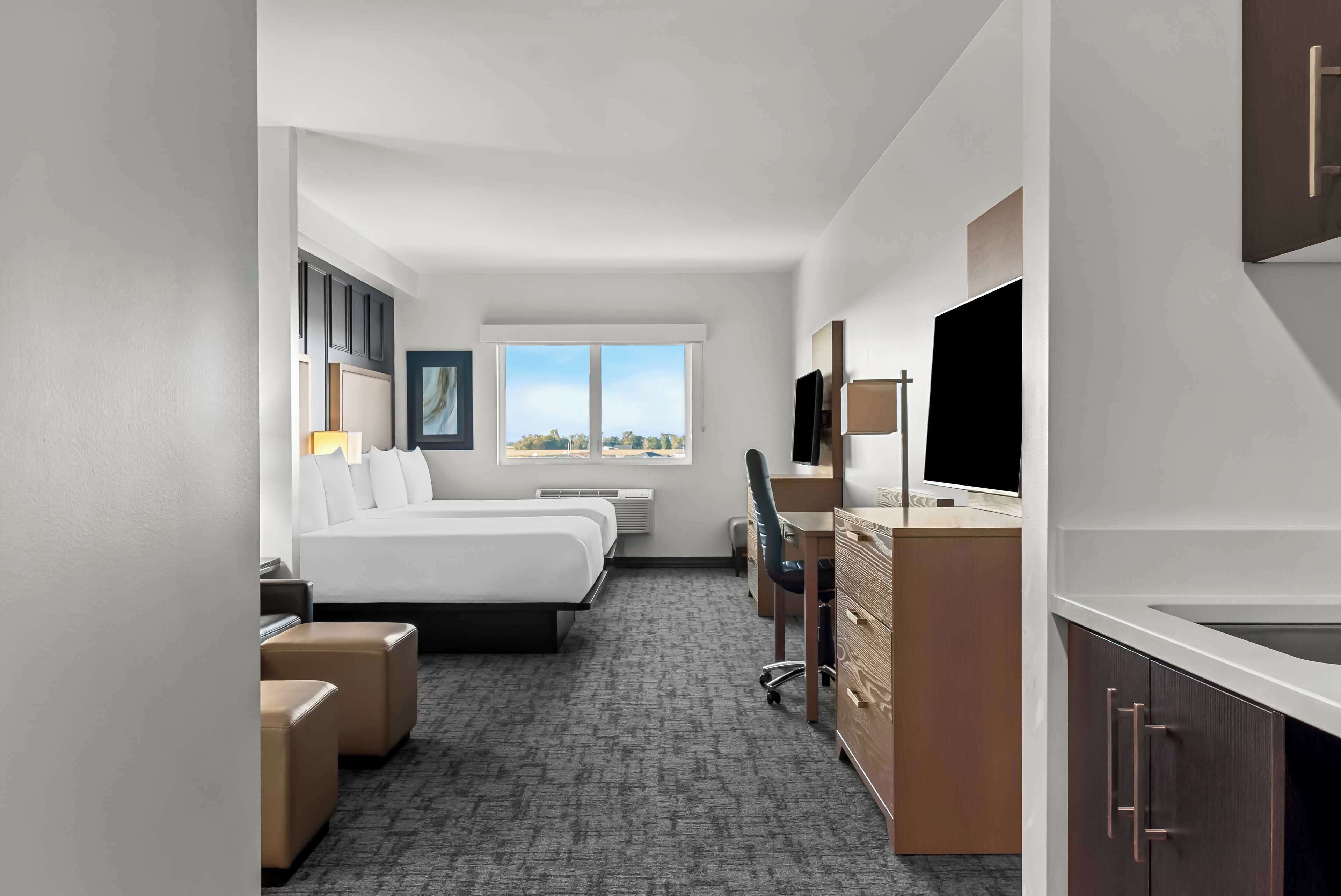 Habitación de hotel con dos camas, un escritorio, una silla, un televisor y una ventana con vista a la ciudad.