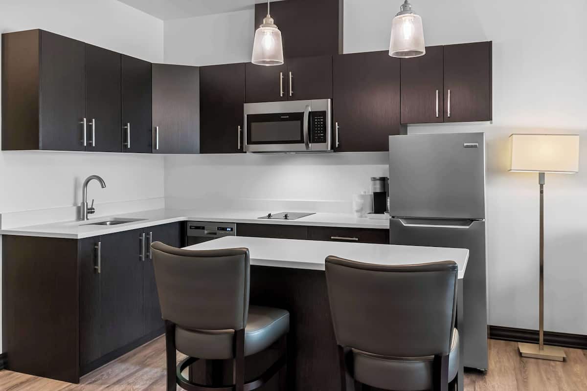 A modern kitchen with dark cabinetry, stainless steel appliances, a central island with bar stools, and pendant lighting.