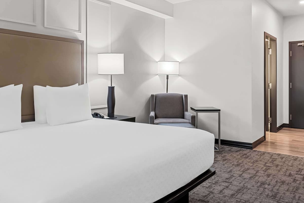 A hotel room with a large bed, two bedside tables, a chair, and a lamp.