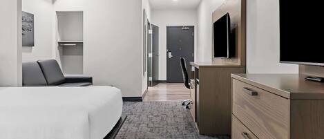 Una habitación de hotel con cama, escritorio, silla, televisor y armario.