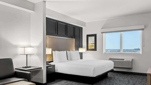 Una habitación de hotel con una cama grande, un escritorio con lámpara, una silla, un ventanal con vistas a la ciudad y un equipo de aire acondicionado.