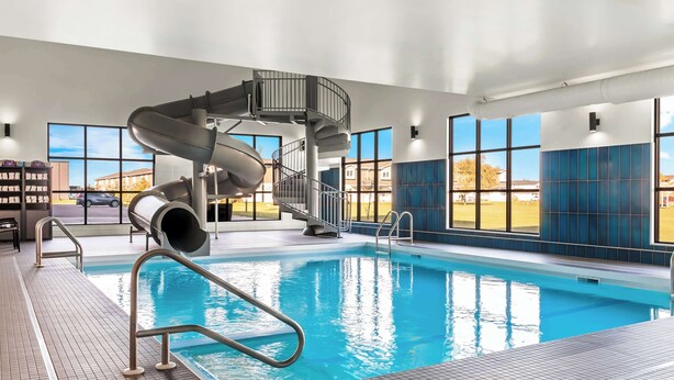 Una piscina interior con tobogán en espiral, ventanas amplias y suelo de baldosas.