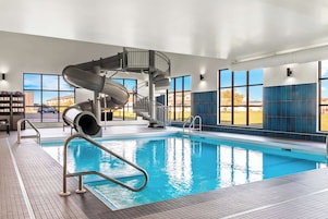 Una piscina interior con tobogán en espiral, ventanas amplias y suelo de baldosas.