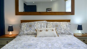 A bedroom with a large mirror, a bed with patterned bedding, two bedside lamps, and a nightstand with a digital clock. - 1 bedroom accommodation in St Bees, near Whitehaven (St Bees, near Whitehaven)