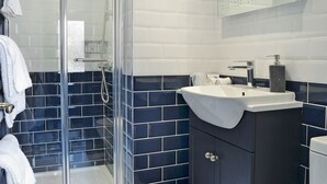A modern bathroom with a glass shower enclosure, a white sink, dark blue tiles, and a dark wooden cabinet. - 1 bedroom accommodation in St Bees, near Whitehaven (St Bees, near Whitehaven)