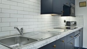 A kitchen with white brick backsplash, dark cabinets, a stainless steel sink, and a microwave. - 1 bedroom accommodation in St Bees, near Whitehaven (St Bees, near Whitehaven)