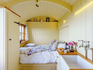 Quarto com cama, janela com cortinas, prateleira com objetos decorativos e banheiro com pia e espelho.
