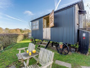 A small, single-story wooden structure with a door open, a bench, and a table with drinks. - 1 bedroom accommodation in Hassocks (Hassocks)