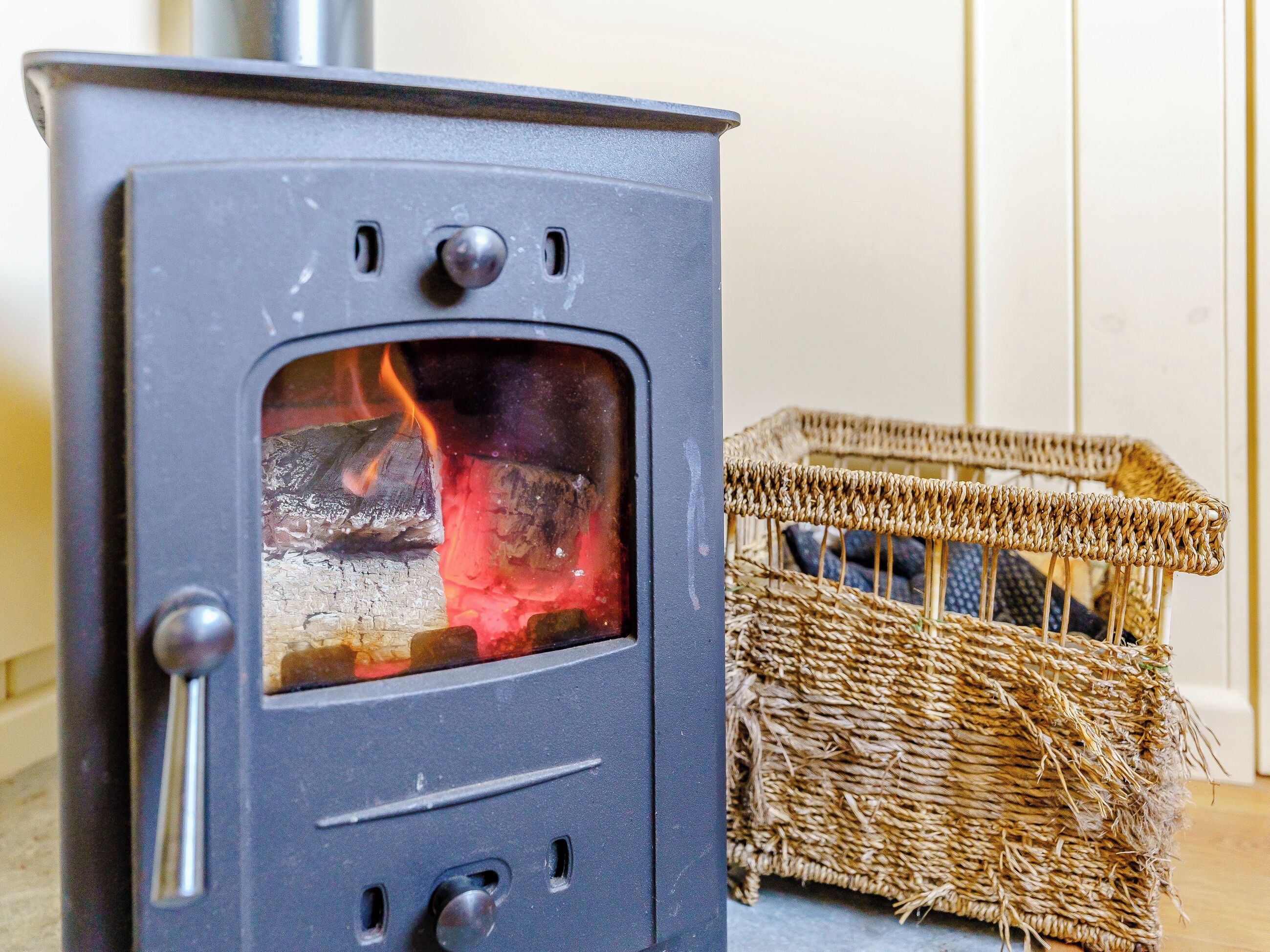 A wood-burning stove with a basket of firewood beside it.